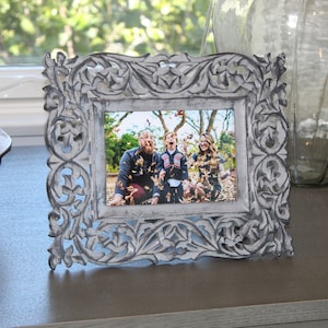 May include: A white carved wooden picture frame with a photo of a family of three in a fall setting. The family is smiling and throwing leaves in the air.