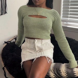 May include: A green crocheted crop top with a cutout detail. The top has long sleeves and a relaxed fit.