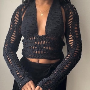 May include: Black crochet halter top with long sleeves. The top features a deep V-neck and openwork detailing on the sleeves and bodice. The garment is handmade and has a unique, textured appearance.