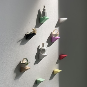 May include: A collection of miniature decorative objects displayed on colorful triangular shelves attached to a white wall. The objects include vases, baskets, and other small sculptures. The shelves are painted in various colors, including green, pink, and red.