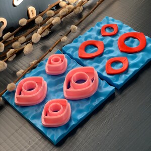 May include: Two blue mats with pink and red cookie cutters in the shape of eyes. The cutters are arranged in a pattern on the mats.