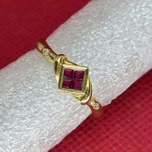 Puede incluir: Un anillo de oro con una piedra preciosa de rubí cuadrada y pequeños diamantes engastados en la banda.