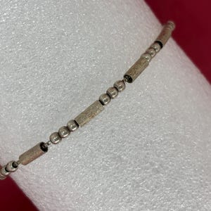 May include: A silver bracelet with alternating round and rectangular beads.