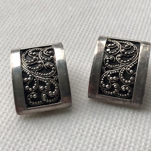 May include: A pair of silver earrings with a filigree design. The earrings are rectangular in shape and have a detailed pattern of swirls and dots.