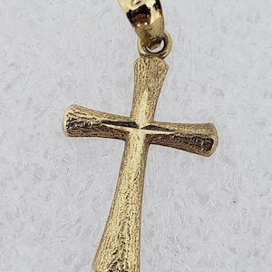 May include: A gold-colored cross pendant with a textured surface. The cross has a traditional design with a loop at the top for a chain. The pendant is likely made of gold and is suitable for religious or fashion purposes.