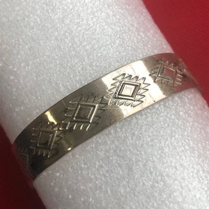 May include: A silver bracelet with a geometric pattern of squares and triangles.