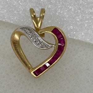 Könnte beinhalten: Goldener herzförmiger Anhänger mit einer Welle aus kleinen Diamanten und einer Reihe rechteckiger Rubine. Der Anhänger hat eine Schlaufe für eine Kette, vor weißem Hintergrund.