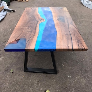 May include: A rectangular wooden table with a river of blue resin running through the center. The table has a dark wood grain and sits on black metal legs. The resin river is a gradient of blues.