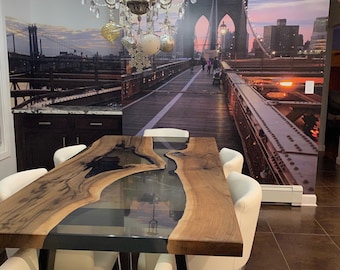Könnte beinhalten: Ein Esstisch aus Holz mit natürlicher Kante und einem schwarzen Epoxidharz-Fluss-Design, getragen von schwarzen Metallbeinen. Weiße Stühle umgeben den Tisch. Ein großer Kronleuchter hängt darüber. Ein Wandbild der Brooklyn Bridge befindet sich an der Wand.