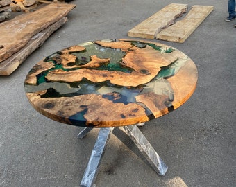 May include: A round wooden table with a unique epoxy resin design. The tabletop features natural wood grain with areas of clear and teal-colored resin. The table has a metal base with four legs. The table is approximately 36 inches in diameter.