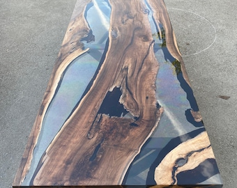 Könnte beinhalten: Ein rechteckiger Holztisch mit dunkelbraunem Finish und einem Flussdesign aus klarem Epoxidharz. Der Tisch hat eine einzigartige, natürliche Holzmaserung und steht auf einem schwarzen, sternförmigen Gestell. Der Tisch ist etwa 183 cm lang.