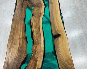 May include: A rectangular wooden table with a live edge design. The table features a teal-colored epoxy resin river running through the center, creating a striking contrast with the natural wood grain. The table measures approximately 72 inches long and 36 inches wide.