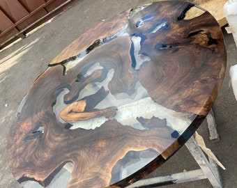 May include: A round wooden table with a dark brown wood grain and a clear epoxy resin finish. The table is supported by a metal frame. The table's diameter is approximately 48 inches.