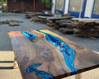 May include: A handcrafted wooden table with a river of vibrant blue epoxy resin flowing through the center. The table has a natural wood grain finish and is supported by metal legs. The table measures approximately 72 inches long.