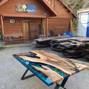 May include: A rectangular wooden table with a live edge design and a blue-green epoxy resin river. The table has a dark wood grain and sits on a black metal X-shaped base. The table measures approximately 72 inches long.