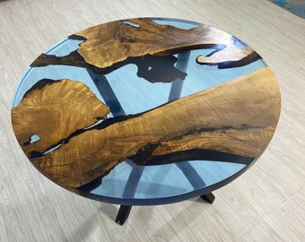 May include: Round coffee table with a unique design. The table features a light blue resin center with natural wood grain patterns and dark wood legs. The wood has a warm brown tone, creating a striking contrast with the blue resin.