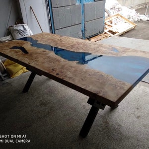 Pode incluir: Mesa retangular de madeira com design de rio de resina azul. A mesa tem um acabamento natural de gr&atilde;o de madeira e pernas de metal preto. A mesa tem aproximadamente 183 cm de comprimento e 91 cm de largura.