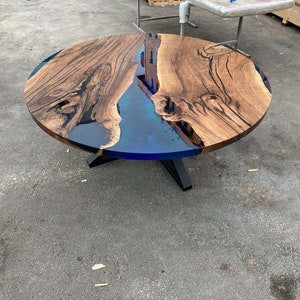 May include: A round wooden table with a blue epoxy resin center. The table has a dark brown wood grain pattern and sits on a black metal base. The table's diameter is approximately 48 inches.