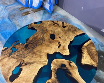 May include: A round coffee table with a unique design. The table features a wooden top with a natural, light brown grain pattern, and a vibrant blue epoxy resin filling the spaces. The table's diameter is approximately 36 inches.