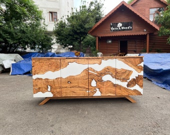 May include: A wooden sideboard with a unique design. The cabinet features a light brown wood grain pattern with white resin accents. The cabinet has four doors and sits on angled wooden legs. The business name "Dara Wood's" is visible in the background.