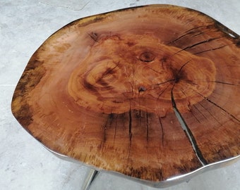 May include: A unique, handcrafted wooden table with a natural, organic shape. The tabletop is a cross-section of a tree trunk, showcasing the wood's grain and knots. The table has a clear, glossy finish and is supported by metal legs.