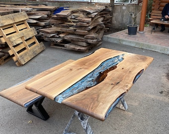 May include: A handcrafted wooden table with a blue resin river design. The table features a natural wood grain and is supported by a metal base. The table measures approximately 72 inches long and 36 inches wide.