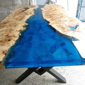 Pode incluir: Mesa retangular de madeira com design de rio em resina ep&oacute;xi azul. A mesa apresenta um tampo de gr&atilde;o de madeira natural com um centro azul vibrante, suportado por pernas de metal preto. As dimens&otilde;es da mesa n&atilde;o s&atilde;o vis&iacute;veis.
