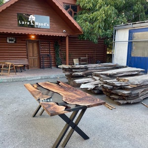 May include: A handcrafted wooden table with a dark epoxy river. The table has a natural wood grain finish and sits on black metal cross legs. The table is approximately 72 inches long and 36 inches wide.