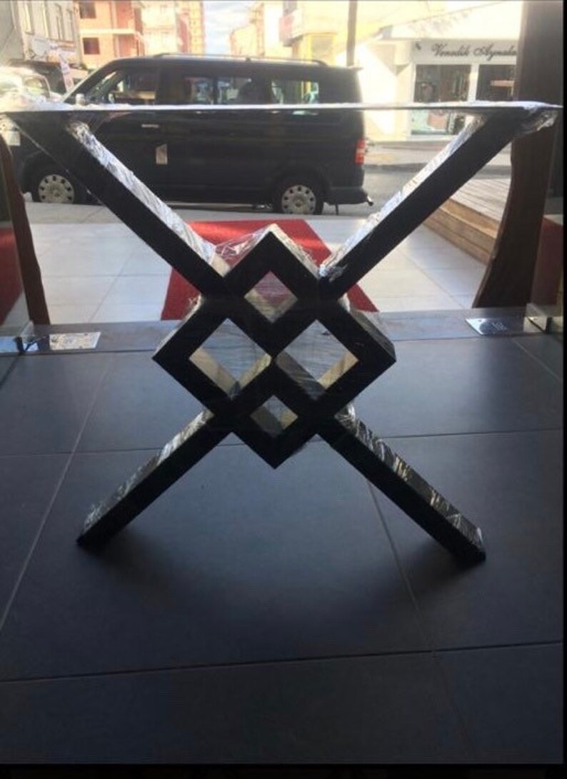 Pode incluir: Base de mesa de metal preto com um design geom&eacute;trico. A base apresenta um padr&atilde;o central em forma de diamante com pernas angulares que se cruzam. A base da mesa &eacute; envolvida em pl&aacute;stico protetor.