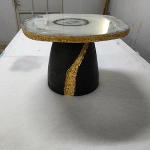 Puede incluir: Una mesa auxiliar única con una tapa redonda estilo ágata. La mesa presenta una base negra con un acento de pan de oro y un borde dorado. La mesa tiene aproximadamente 50 cm de diámetro y 50 cm de altura.