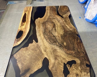 May include: A rectangular coffee table with a live edge wood design. The table features a natural wood grain pattern with dark epoxy resin filling the voids. The edges are rounded and the table has a glossy finish.
