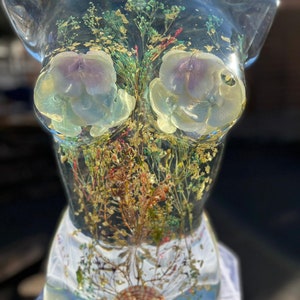 Puede incluir: Escultura de torso de resina transparente, con flores secas, l&aacute;minas de oro y una concha. Las flores son de varios colores. Una pieza de arte decorativa.