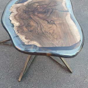 May include: A unique, handcrafted coffee table with a live edge wood top encased in clear resin. The wood grain is visible, and the table is supported by gold-colored metal legs. The table's dimensions are approximately 30 inches long, 20 inches wide, and 18 inches high.