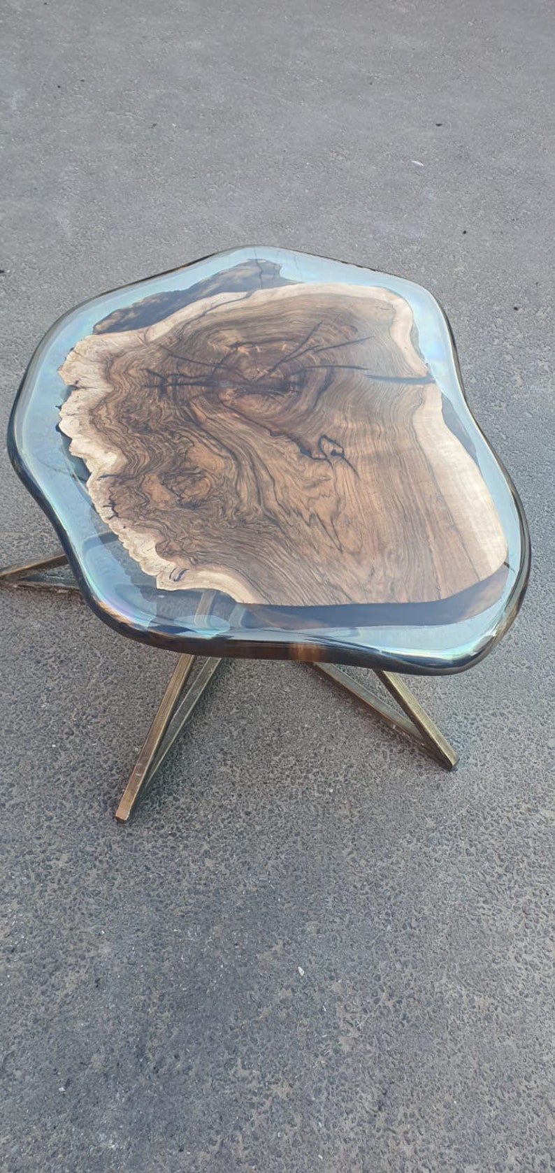 May include: A unique, handcrafted coffee table with a live edge wood top encased in clear resin. The wood grain is visible, and the table is supported by gold-colored metal legs. The table's dimensions are approximately 30 inches long, 20 inches wide, and 18 inches high.