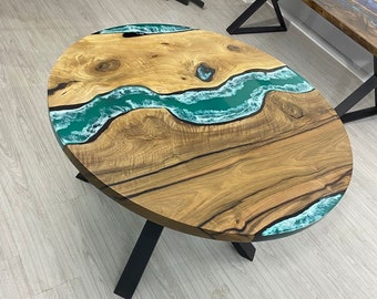May include: Oval wooden coffee table with a teal epoxy river design. The table has a natural wood grain finish and black metal legs. The epoxy river flows through the center, creating a unique and artistic look.