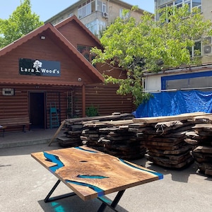 May include: A handcrafted wooden table with a live edge design and a vibrant blue epoxy resin river. The table is supported by black metal legs. The table measures approximately 72 inches long and 36 inches wide.