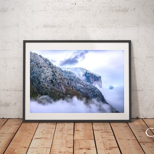 May include: A framed photograph of a snow-capped mountain range with clouds in the valley below. The mountain peaks are covered in snow and the clouds are a soft white.