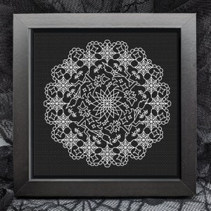 May include: A black framed embroidery hoop with a white mandala design featuring geometric shapes and stars. The design is reminiscent of a spiderweb.