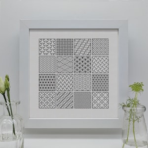 Puede incluir: Una impresión enmarcada en blanco con un diseño de patrón geométrico en blanco y negro. La impresión está dividida en 16 cuadrados, cada uno con un patrón diferente.
