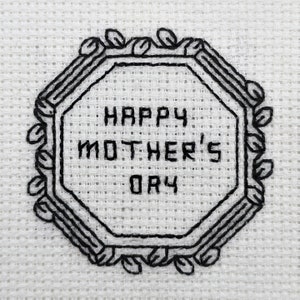 Pode incluir: Tecido branco com bordado preto de um oct&oacute;gono com o texto "Happy Mother's Day" dentro.