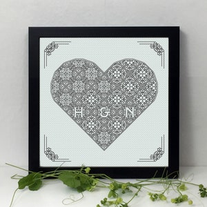 May include: A black framed embroidery hoop with a white background and a black heart design. The heart is filled with a geometric pattern and the initials "H & N" are in the center.