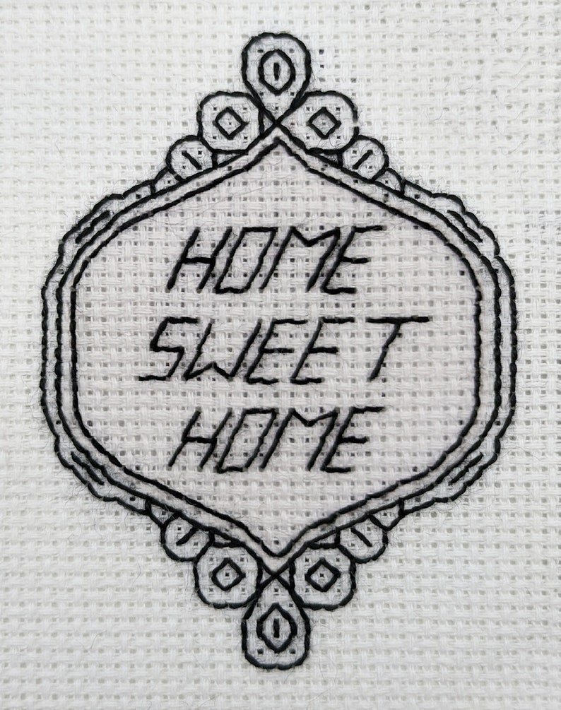 Pode incluir: Desenho bordado em preto e branco sobre um fundo de tecido branco. O desenho apresenta uma moldura decorativa com o texto "HOME SWEET HOME" no seu interior.