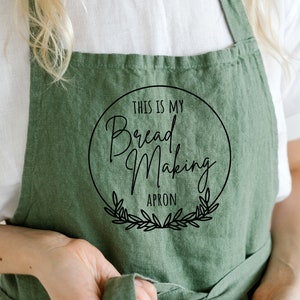 K&ouml;nnte beinhalten: Gr&uuml;ne Leinensch&uuml;rze mit einem schwarzen Kreislogo, auf dem "This is my Bread Making Apron" steht.