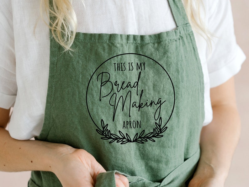 K&ouml;nnte beinhalten: Gr&uuml;ne Leinensch&uuml;rze mit einem schwarzen Kreislogo, auf dem "This is my Bread Making Apron" steht.