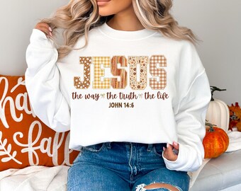 May include: White sweatshirt with the word "JESUS" in a decorative font. The letters are patterned with floral, plaid, and wood grain designs. Below the word "JESUS" is the text "the way the truth the life" and "JOHN 14:6".
