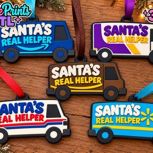 May include: Five van-shaped Christmas ornaments made of flexible material, each featuring the text SANTA'S REAL HELPER. The ornaments come in blue, purple, brown, white, and light blue, each with a colored ribbon loop for hanging on a tree.