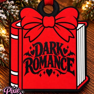 May include: A red book-shaped ornament featuring a large red bow at the top and the black text "DARK ROMANCE" printed on the front cover. The design includes black heart and bat accents, with a black border and a red ribbon loop for hanging.
