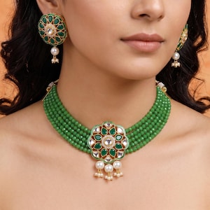 Puede incluir: Un conjunto de collar y pendientes de cuentas verdes. El collar presenta un gran colgante floral con detalles verdes y dorados, y perlas colgantes. Los pendientes tienen un diseño floral similar con una gota de perla.