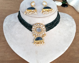 Könnte beinhalten: Eine grüne Perlen-Choker-Kette mit einem goldenen Anhänger, der einen großen, runden, klaren Stein umgeben von kleineren Steinen zeigt. Der Anhänger hat einen kleineren, halbmondförmigen Stein, der daran hängt. Die Kette wird mit einem Paar passender Ohrringe geliefert.