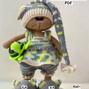 May include: A crocheted doll wearing a long, floppy hat, a sleeveless top, and shorts in a variegated gray, white, and yellow yarn. The doll wears gray slippers with white and yellow ears and holds a small green turtle. Text reads PAJAMA OUTFIT CROCHET PATTERN PDF, Hat, Top, Slippers.